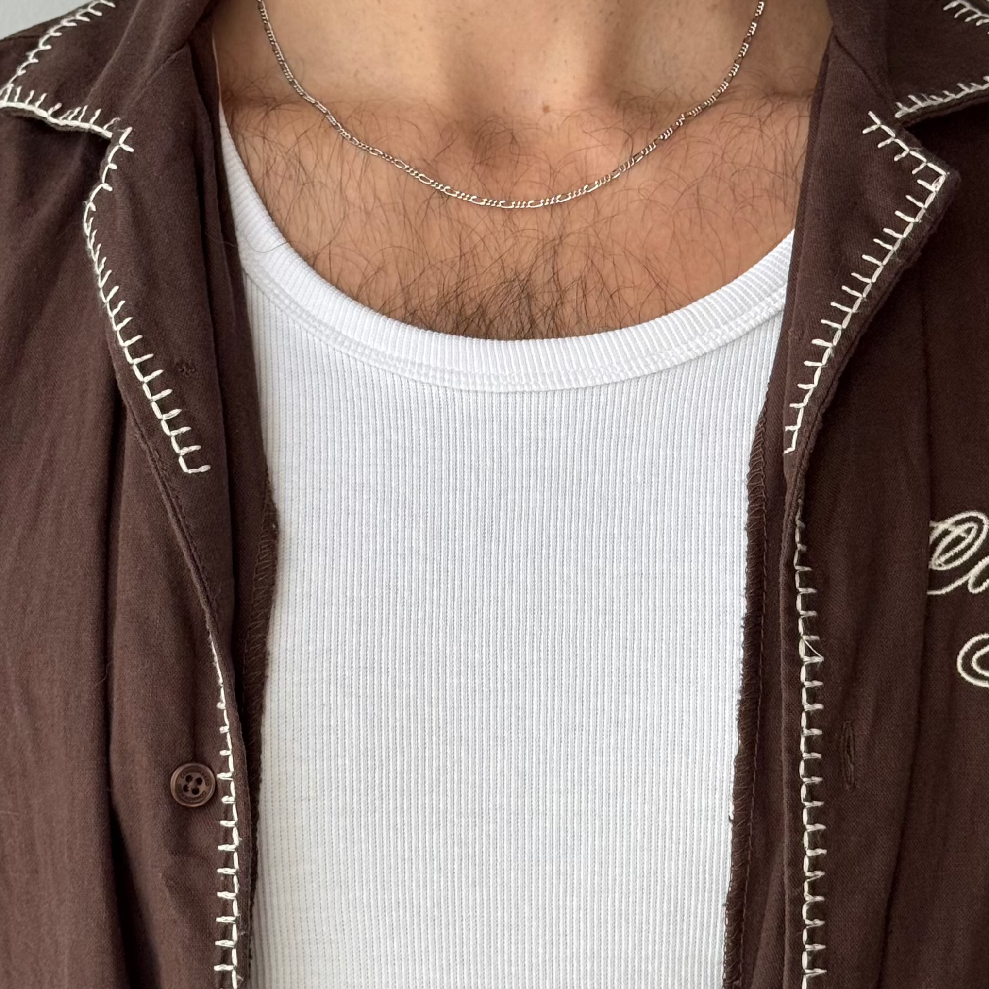 A close-up of the Billie Jo Slim Figaro Necklace in sterling silver, resting on a man's chest, highlighting the intricate link pattern and quality craftsmanship.
