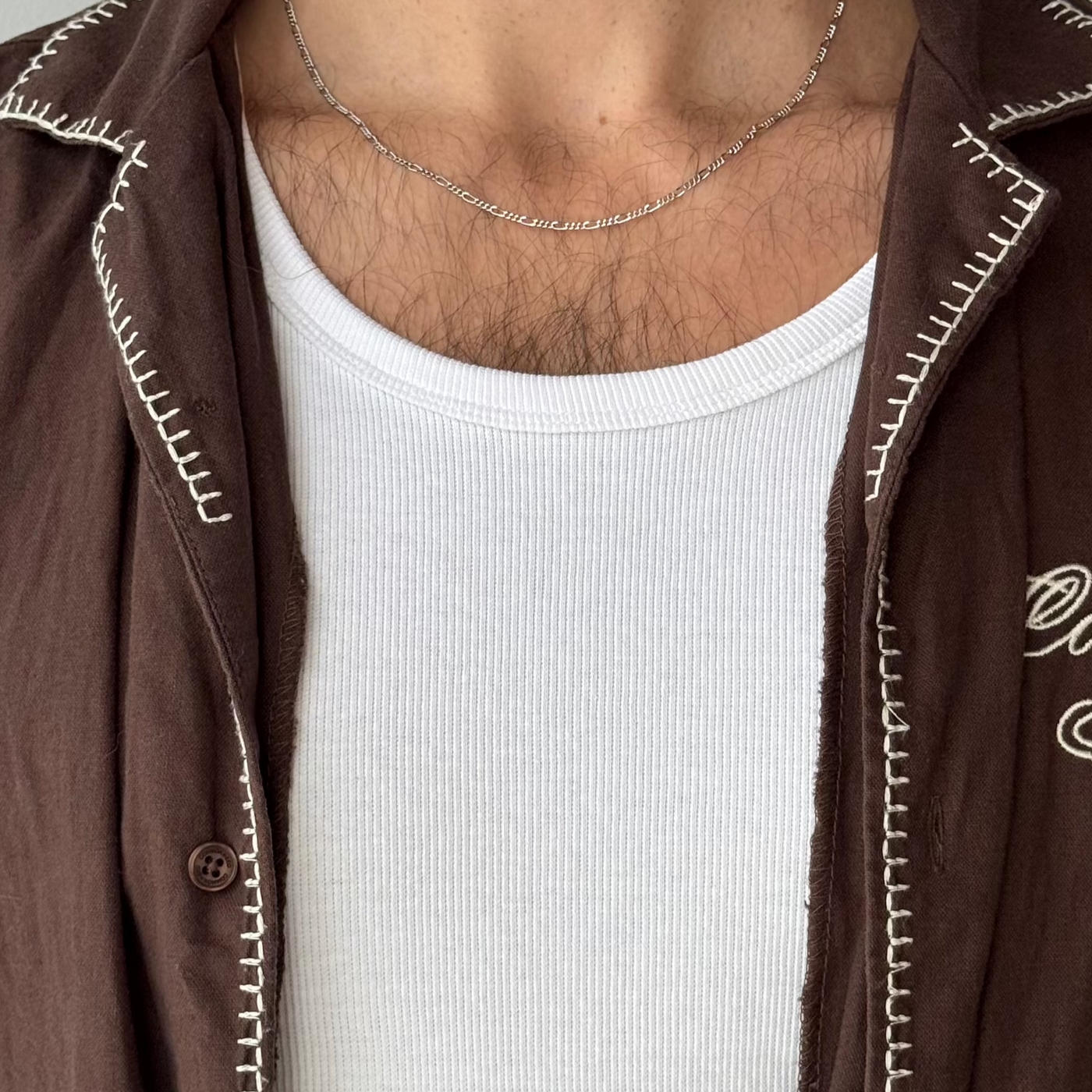 A close-up of the Billie Jo Slim Figaro Necklace in sterling silver, resting on a man's chest, highlighting the intricate link pattern and quality craftsmanship.