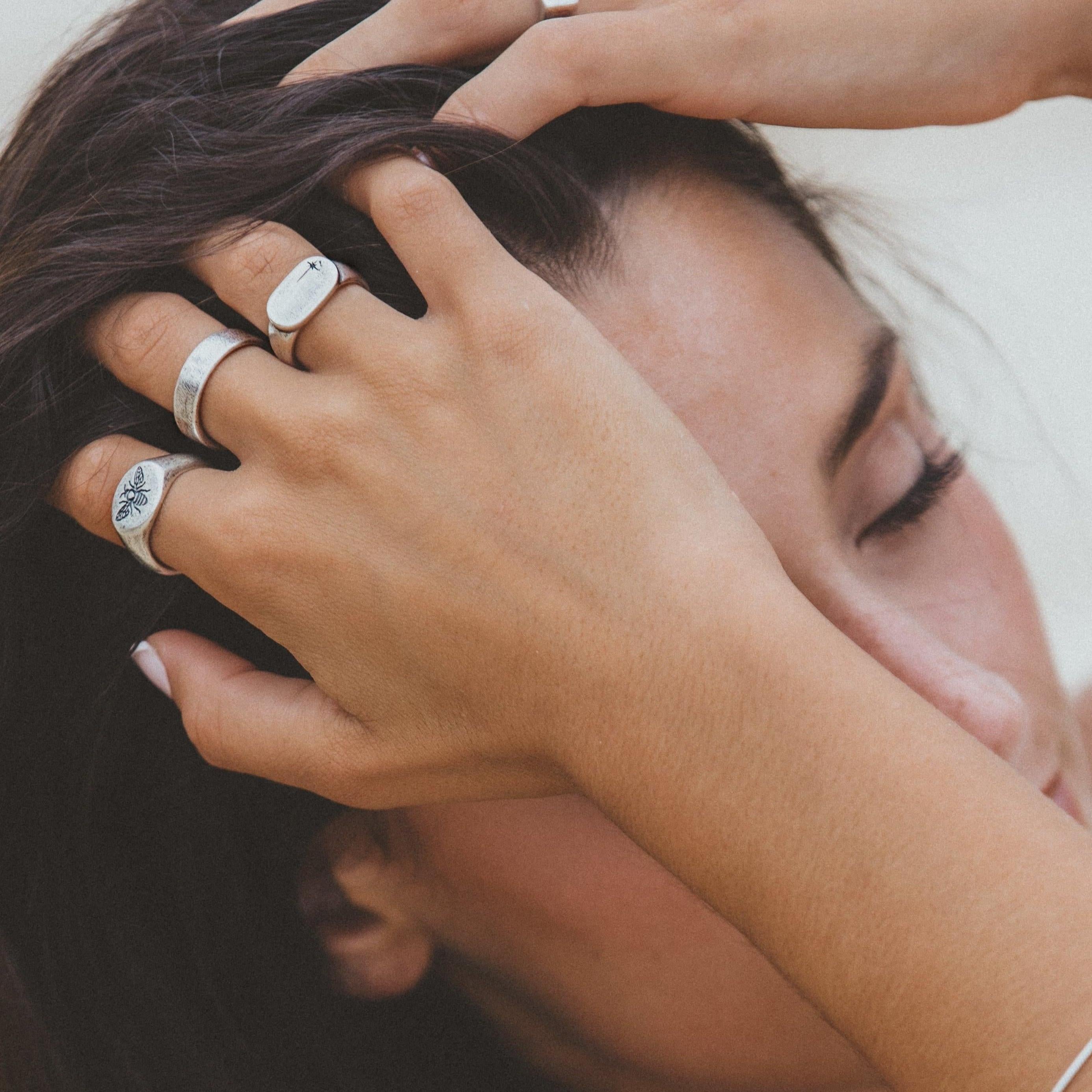 A woman with her hand in her dark hair, wearing the BEE THERE RING and other sterling silver rings from Australian jewellery brand Billie Jo.