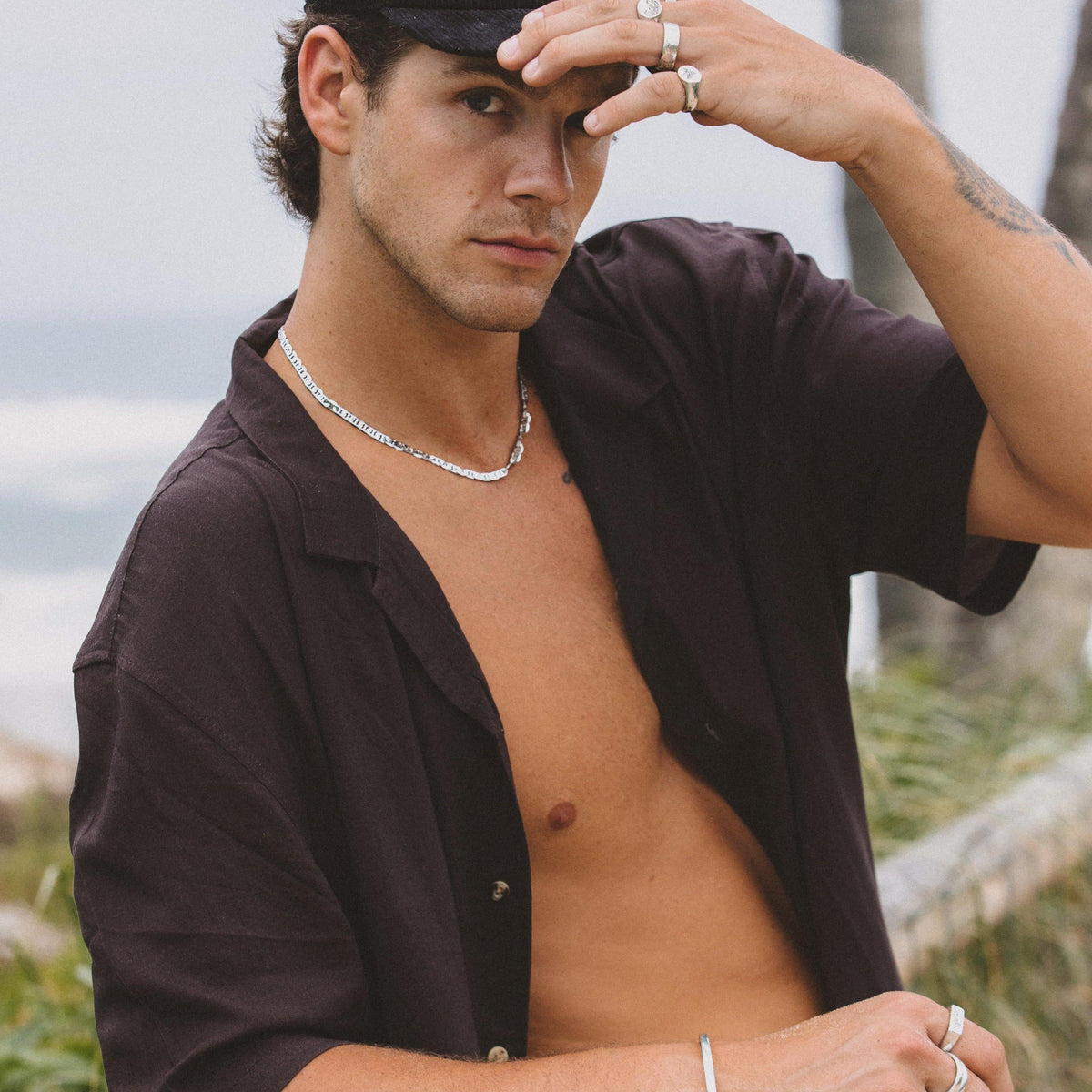 A man wearing the Billie Jo Mariner Necklace, styled with an open black shirt and cap for a relaxed, modern look on the Gold Coast.