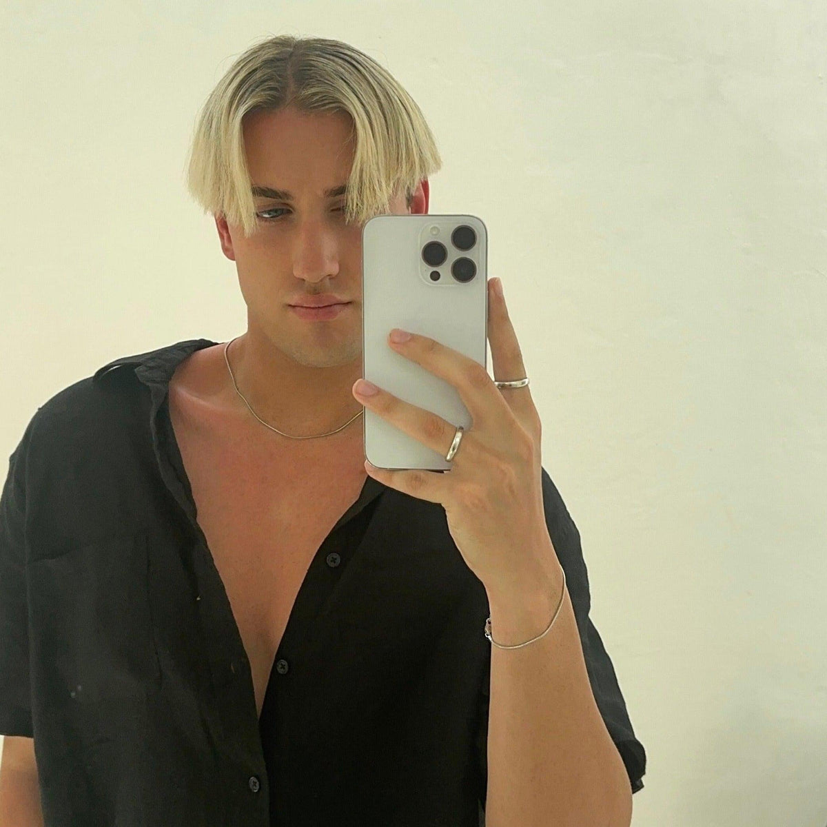 A young man with blond hair takes a mirror selfie, wearing an open black shirt and Billie Jo jewellery. The sterling silver Snake Bracelet is visible on his wrist, showcasing its effortless style for a casual, modern look.