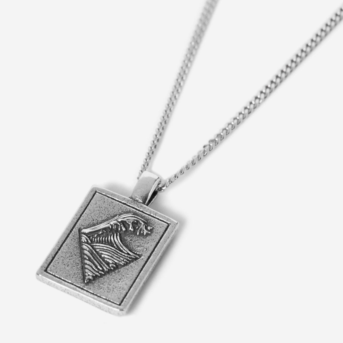 The sterling silver Burleigh Pendant by Billie Jo, featuring a rectangular design with an engraved ocean wave, on a silver chain against a white background.