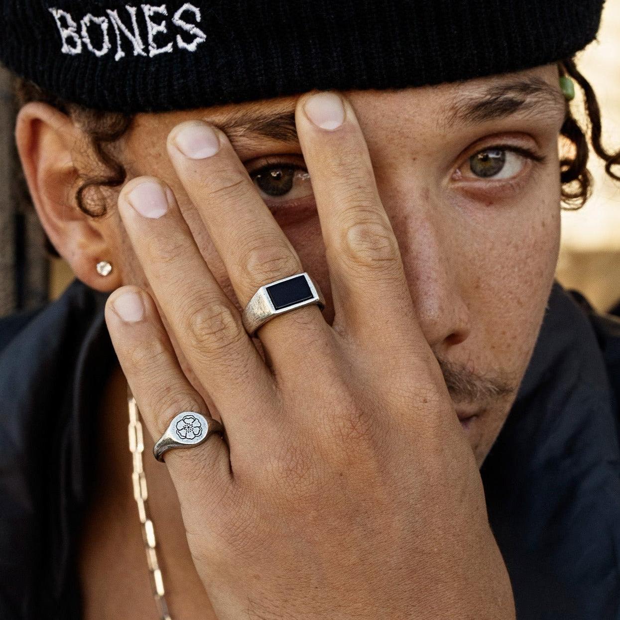 Close-up of a man's hand wearing the sterling silver Solace Ring by Billie Jo, styled with a black beanie and a silver chain. Men's fashion jewellery.