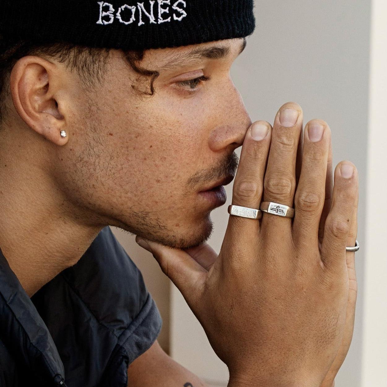 A profile shot of a man in a black beanie, his hand resting on his chin, highlighting the sterling silver Essence Ring from Australian brand Billie Jo.