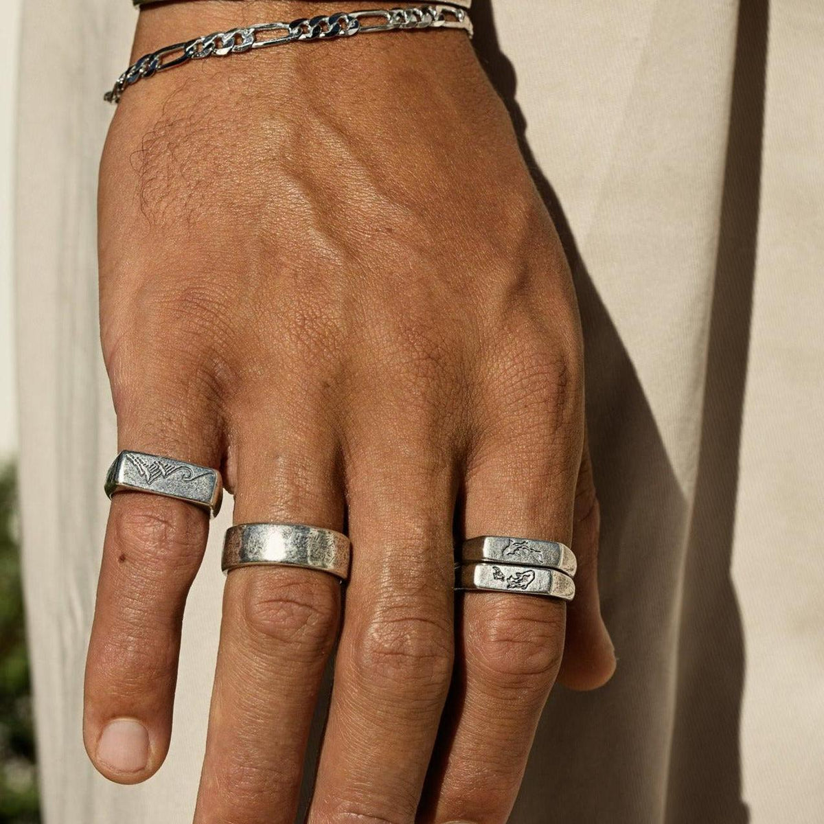 A man's hand wearing the sterling silver Figaro Bracelet and a selection of silver rings from Australian men's jewellery brand Billie Jo. This lifestyle shot shows the bracelet styled with other pieces.