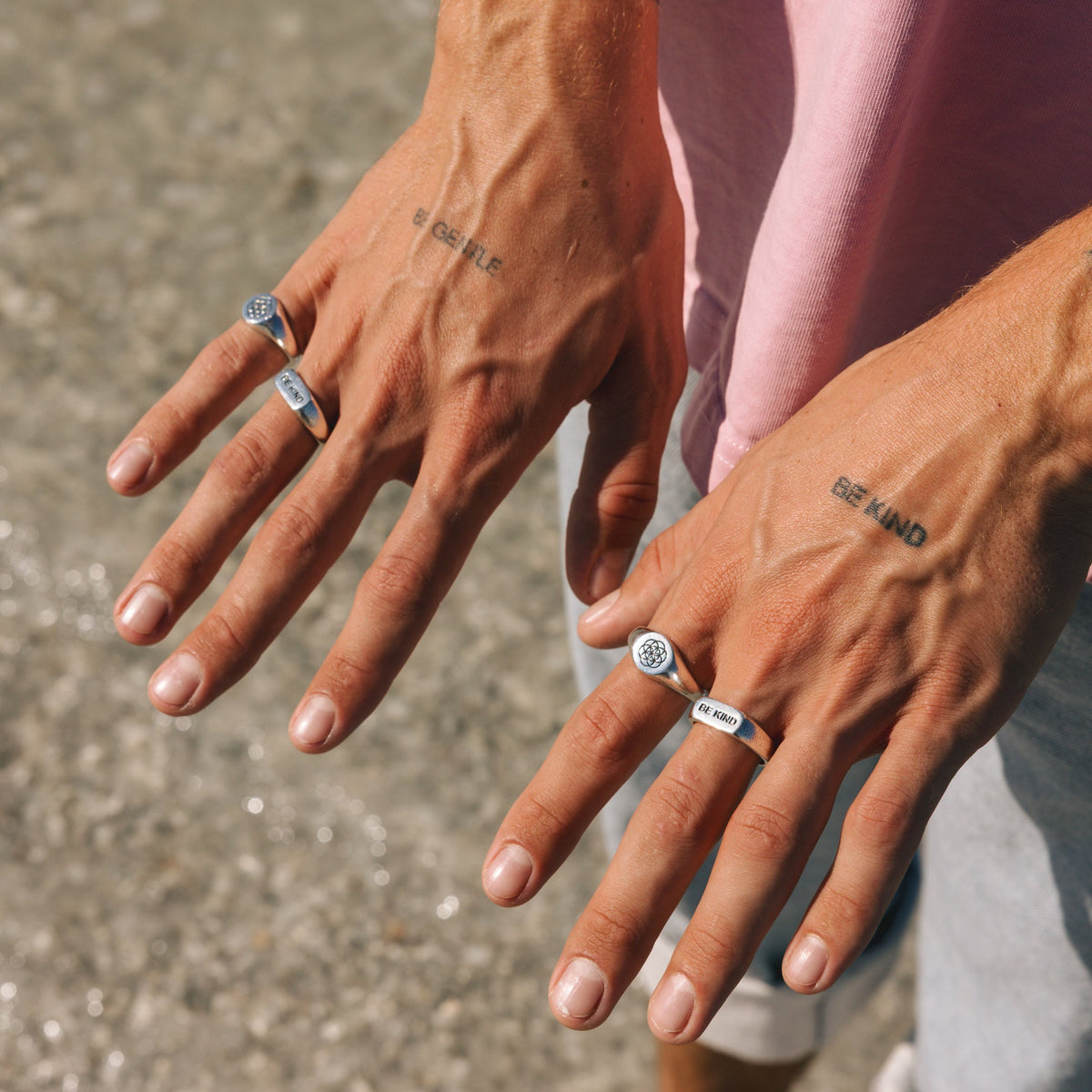 A man's hands showing off a collection of Billie Jo rings, including the BE KIND ring, demonstrating how to stack and style the brand's jewellery.