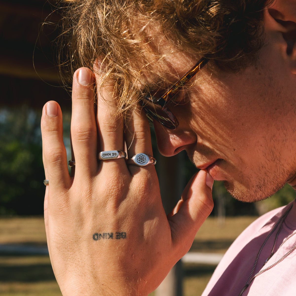 A close-up editorial shot of a man wearing the BE KIND ring, with his hand resting on his face, highlighting the ring's bold and expressive design.