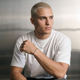 A male model wearing a gold tone stainless steel slim Figaro chain necklace from Australian jewellery brand Billie Jo, shot against a sleek silver chrome backdrop showcasing the delicate alternating link design perfect for everyday wear.