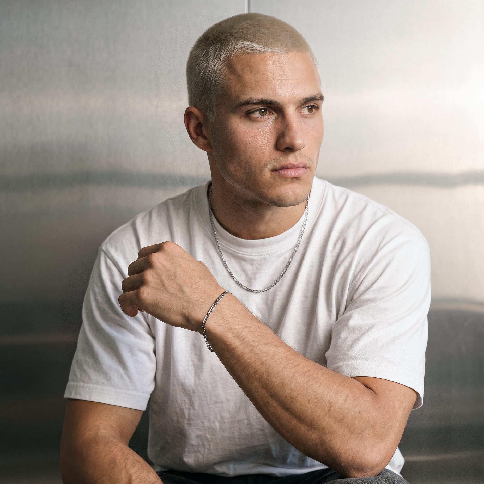 A male model wearing a gold tone stainless steel slim Figaro chain necklace from Australian jewellery brand Billie Jo, shot against a sleek silver chrome backdrop showcasing the delicate alternating link design perfect for everyday wear.