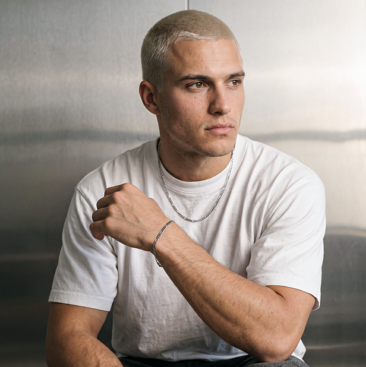 A male model wearing a gold tone stainless steel slim Figaro chain necklace from Australian jewellery brand Billie Jo, shot against a sleek silver chrome backdrop showcasing the delicate alternating link design perfect for everyday wear.