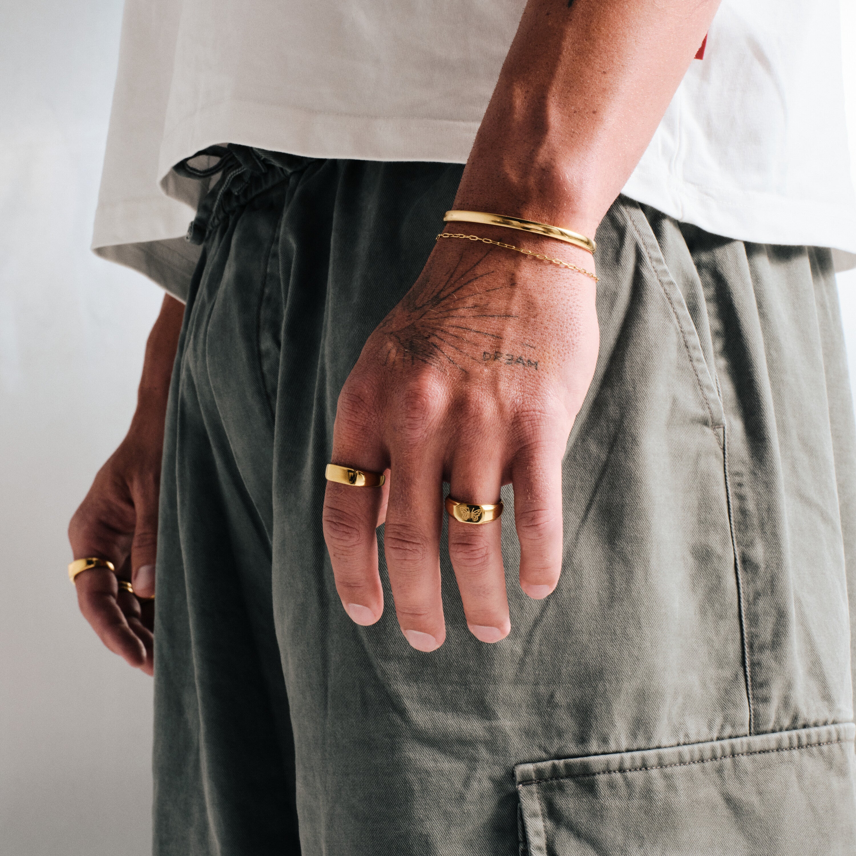 Men's Gold Drifter Cuff in 18k gold infused stainless steel, worn on his left wrist, hand by his side, white tee, olive pants