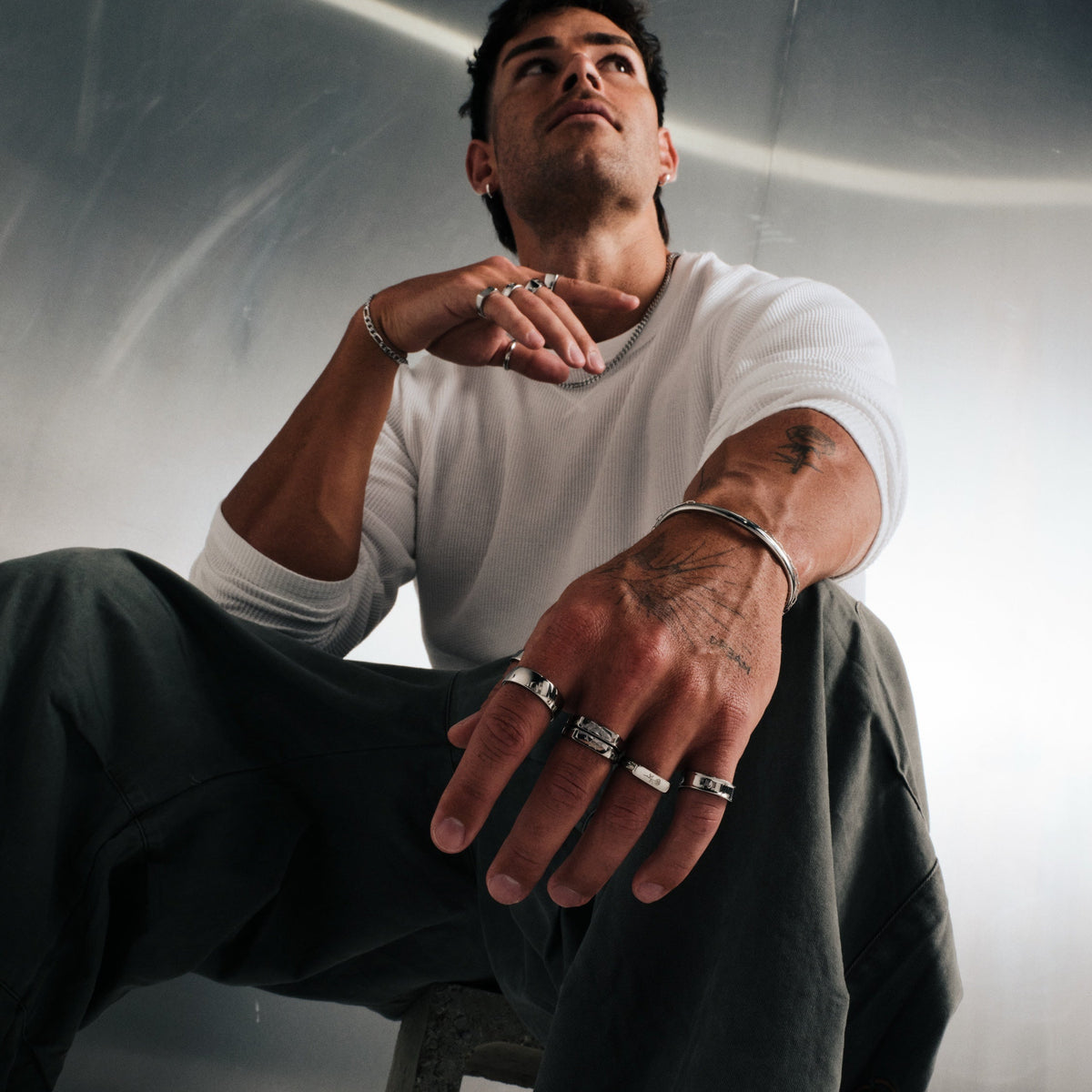 Men's Drifter Cuff in 316L stainless steel, silver finish, worn on his left wrist, seated, low angle, right hand at his chin