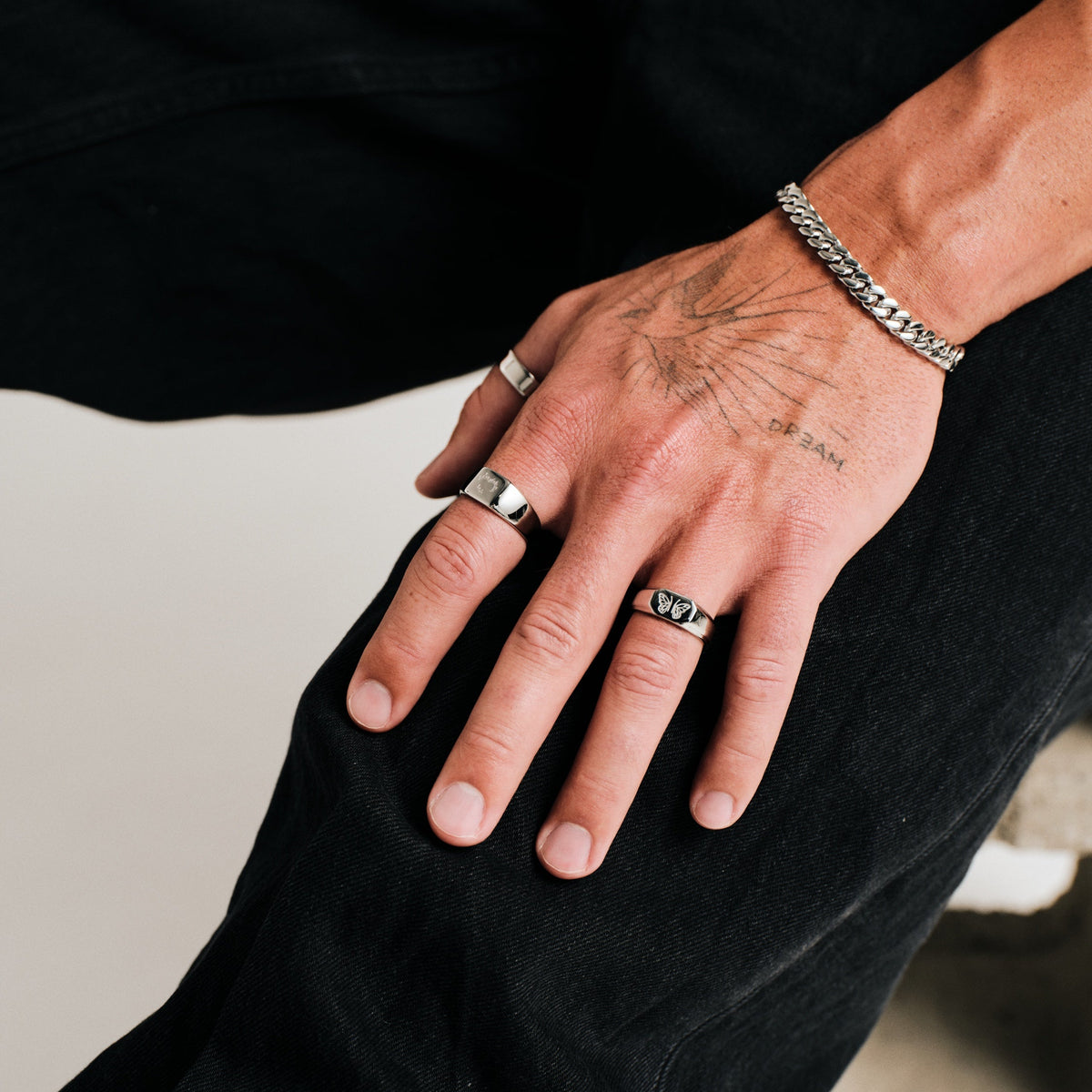 Men's Ember Ring in 316L stainless steel, silver finish, worn on his left index finger, seated, hand resting on his knee