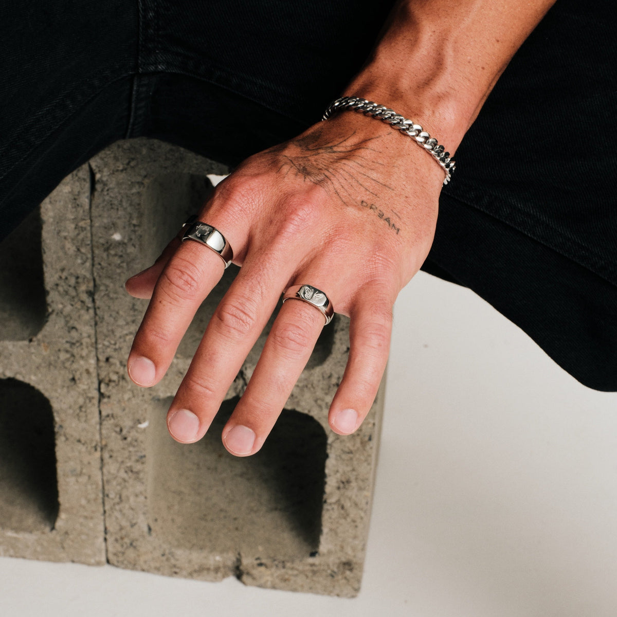 Men's Ember Ring in 316L stainless steel, silver finish, worn on his left index finger, hand resting on a concrete block