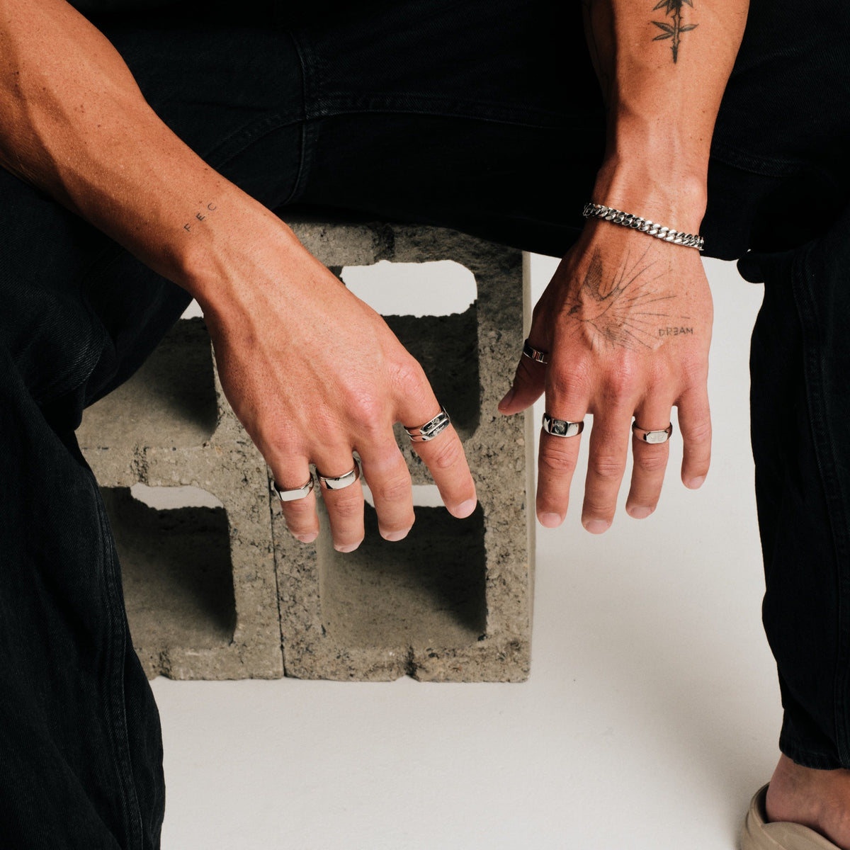 Men's Ember Ring in 316L stainless steel, silver finish, worn on the index finger, seated on a concrete block, hands down