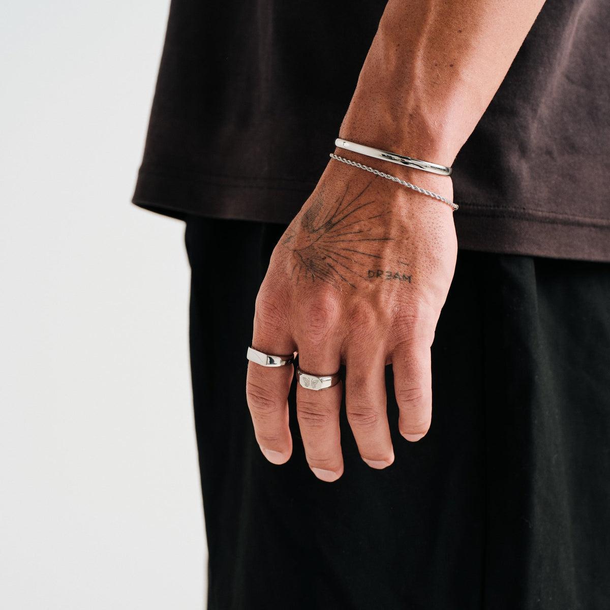 Men's Genesis Ring in 316L stainless steel, silver finish, worn on his left index finger, hand hanging at his side