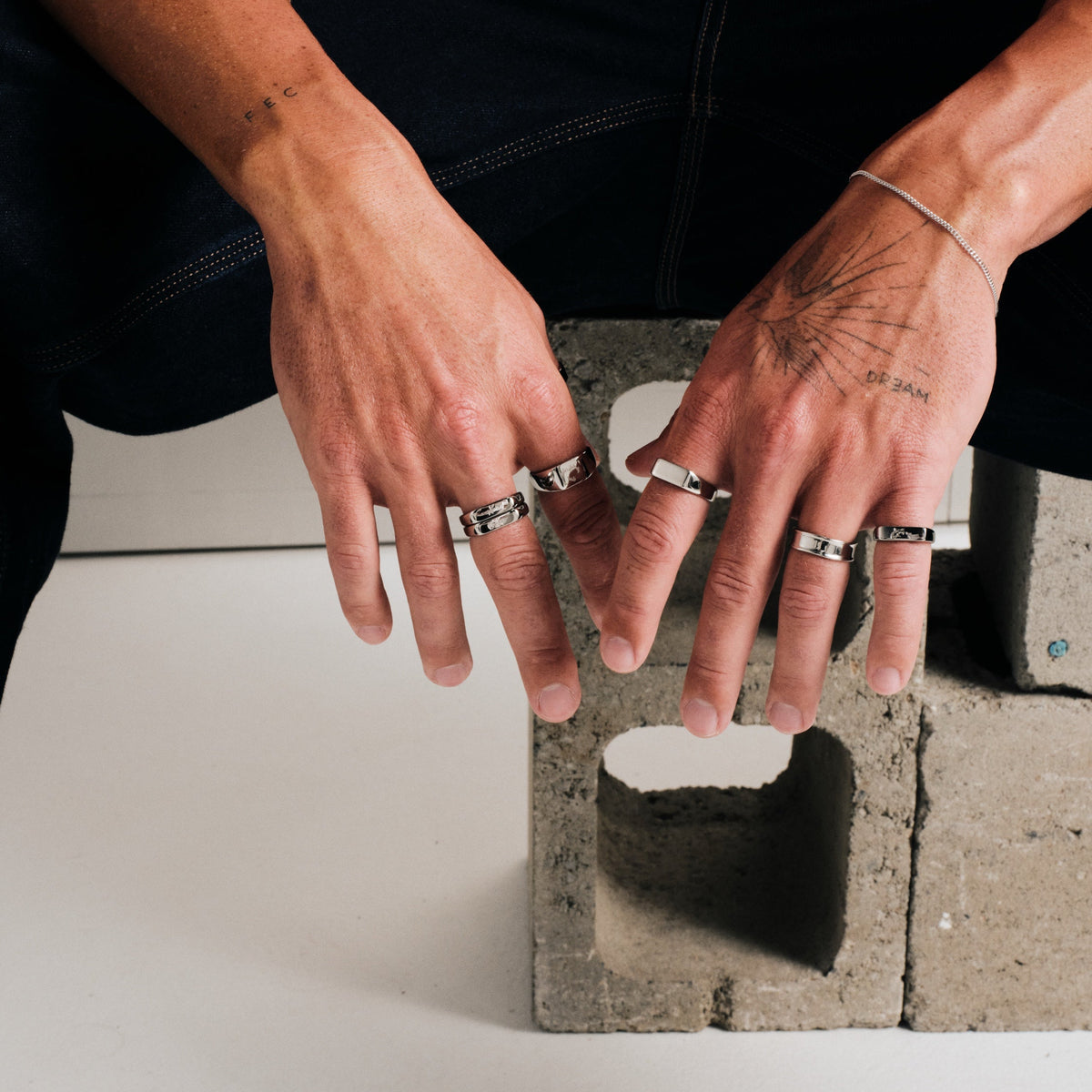 Men's Genesis Ring in 316L stainless steel, silver finish, worn on the index finger, both hands draped over a concrete block