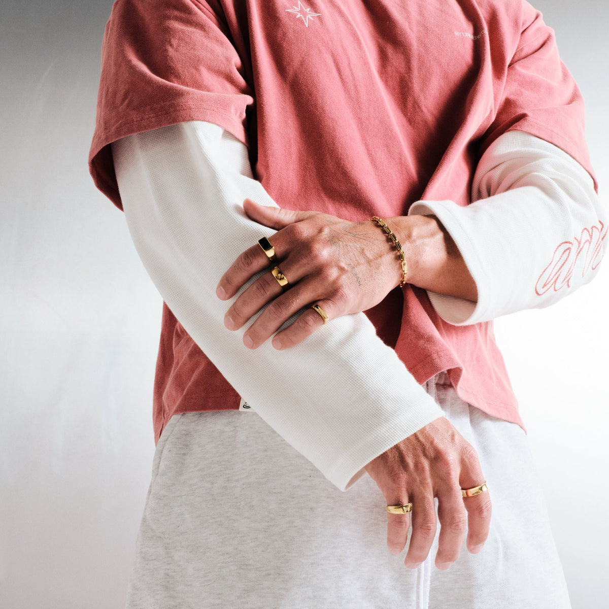 Man wearing gold stainless rings, hand over his forearm, with a gold box link chain bracelet