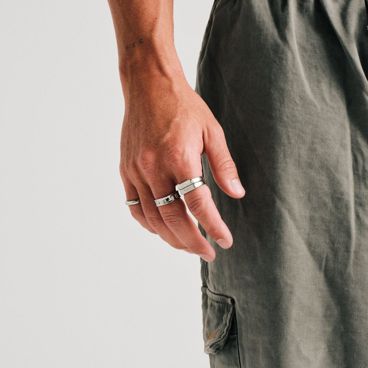 Men's Koi Stackers in 316L stainless steel, silver finish, both worn on his right index finger, hand relaxed at his side