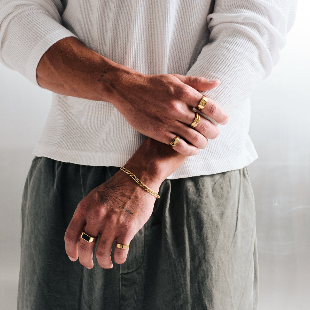Men's Gold Onyx Ring in 18k gold infused stainless steel, worn on the middle finger, arms folded at the waist