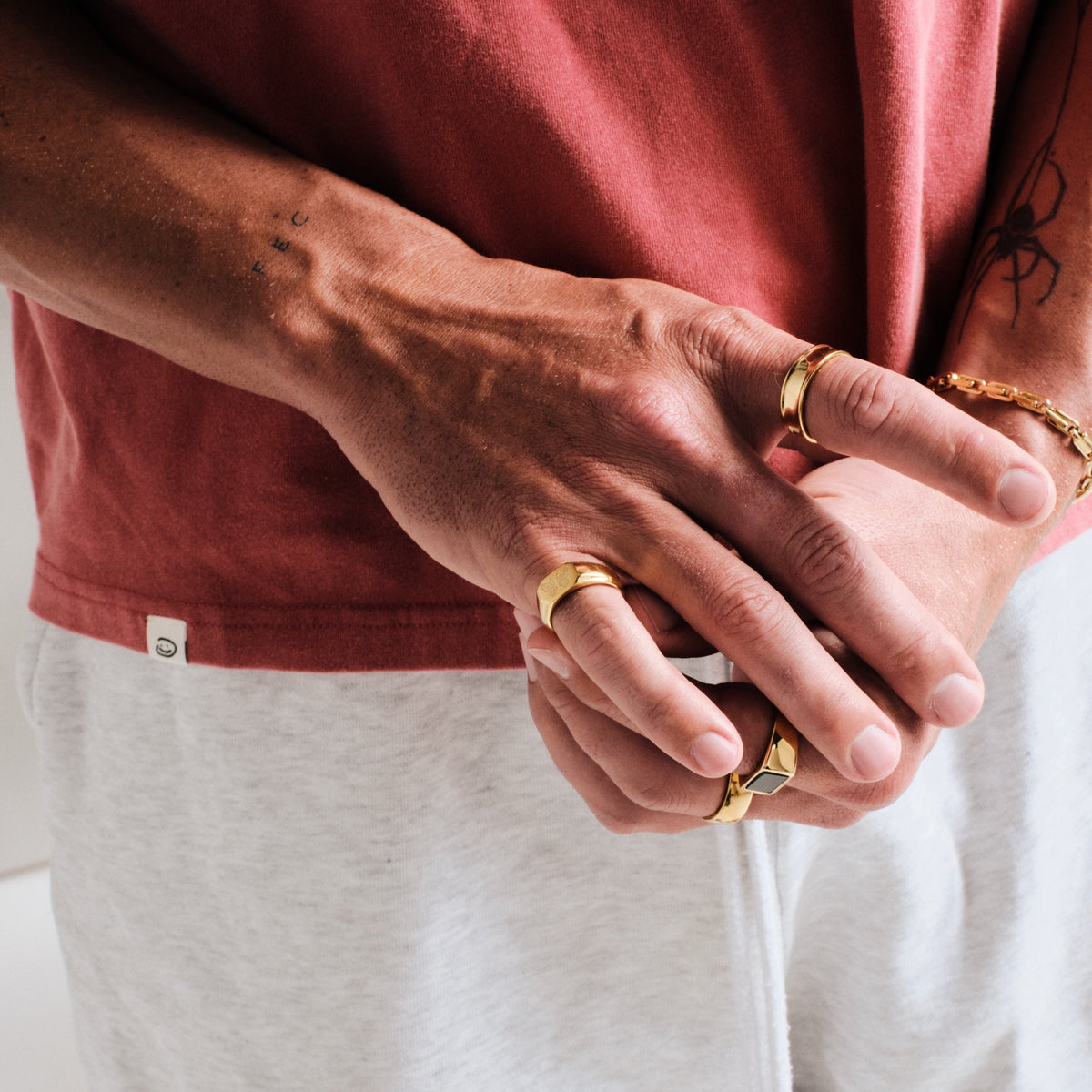 Men's Gold Revival Ring in 18k gold infused stainless steel, worn on the little finger, hands clasped at his waist