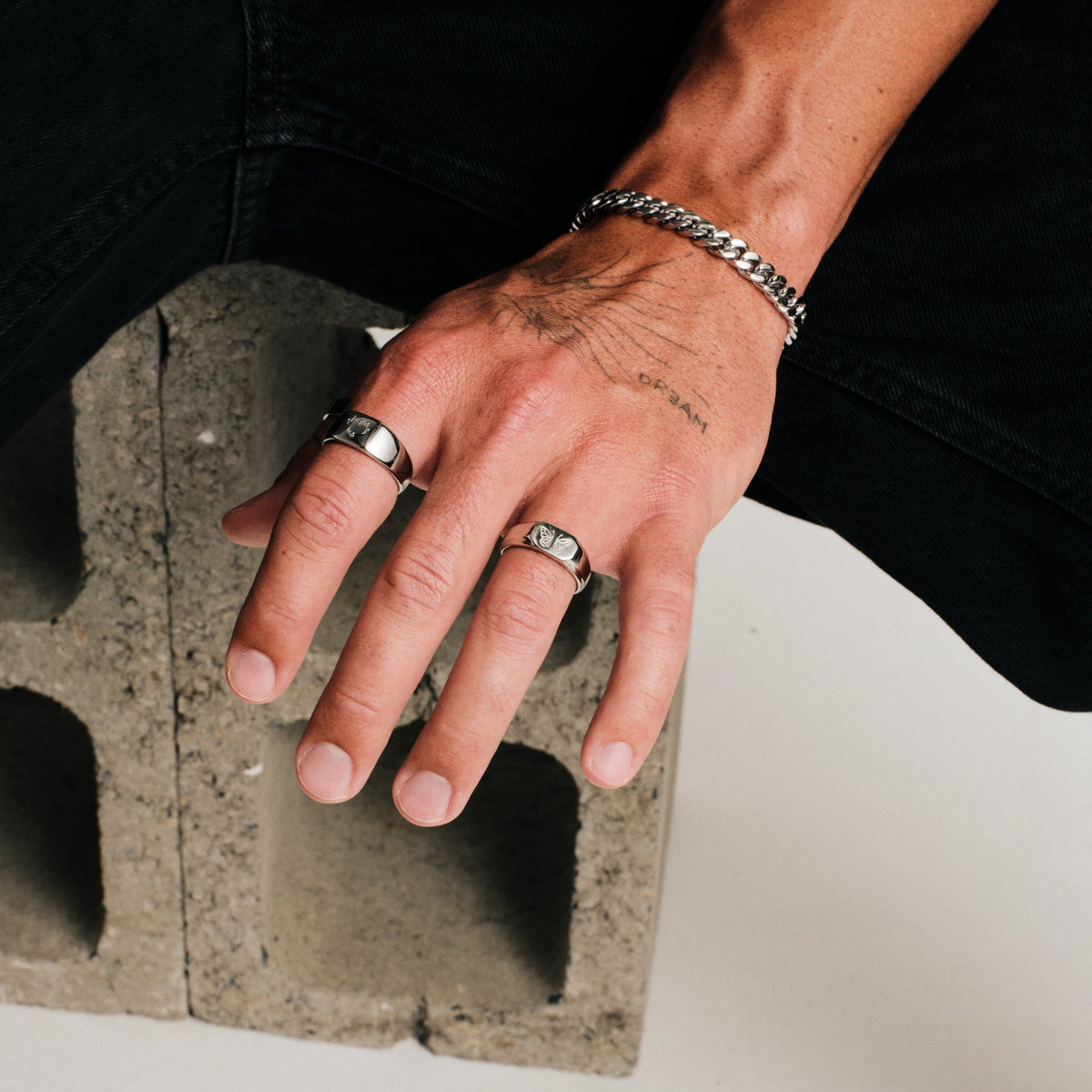 Men's Revival Ring in 316L stainless steel, silver finish, worn on his left ring finger, hand resting on a concrete block