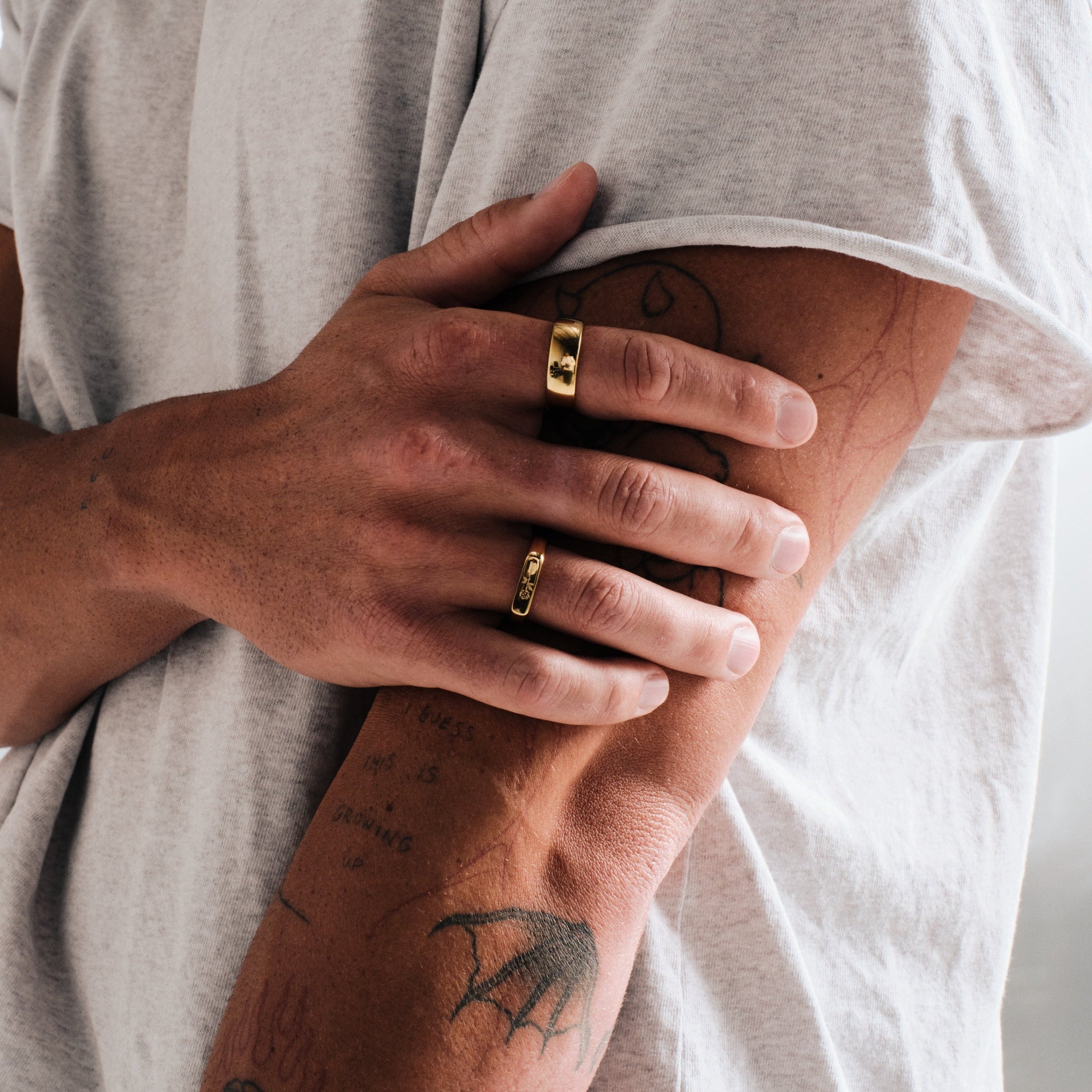 Men's Gold Rosa I Ring in 18k gold infused stainless steel, worn on the index finger, hand gripping his tattooed forearm