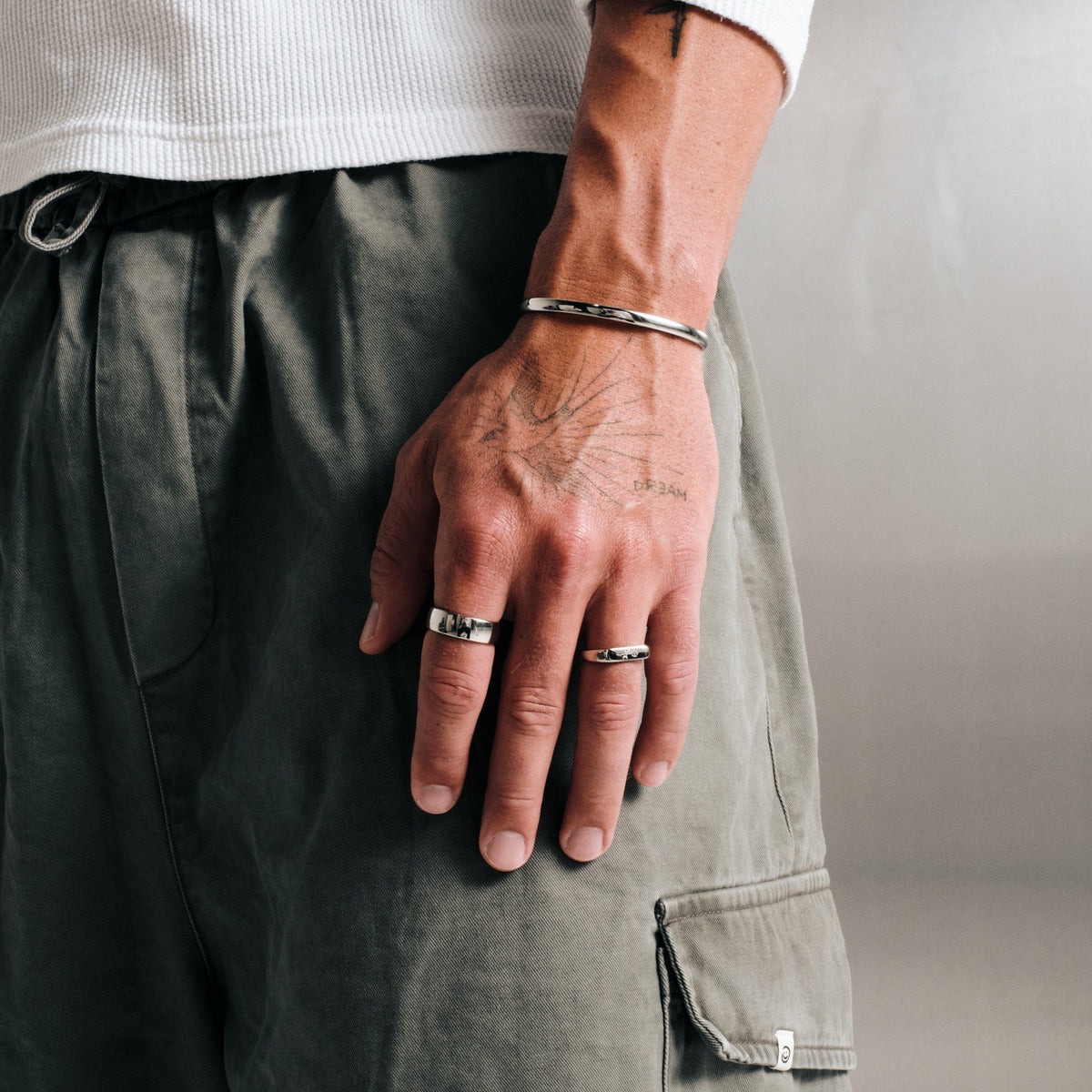 Man wearing silver finish stainless rings, hand by his side, with a steel Drifter Cuff on wrist