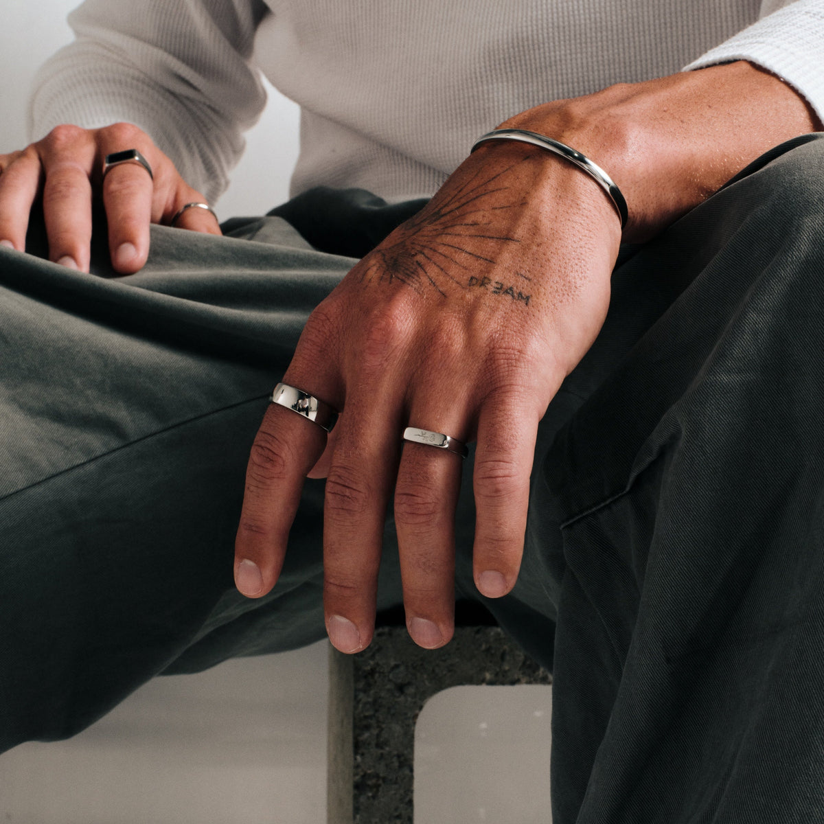 Men's Rosa II Ring in 316L stainless steel, silver finish, worn on the ring finger, seated, hands on his knees