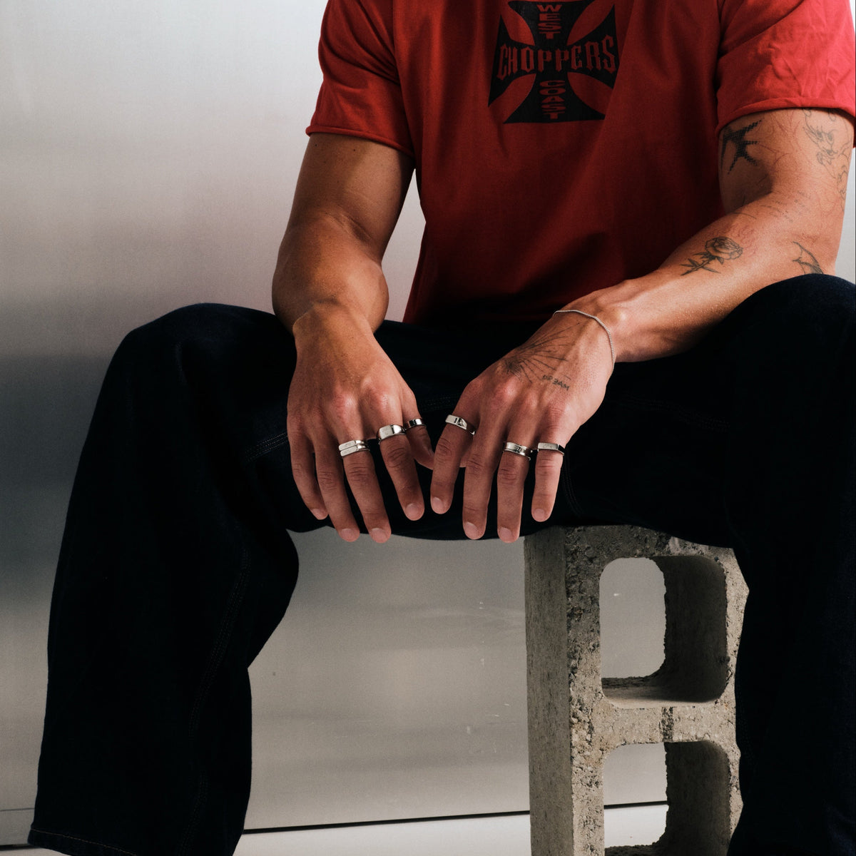 Men's Rosa Stackers in 316L stainless steel, silver finish, in a stack, seated on a concrete block, hands on knees