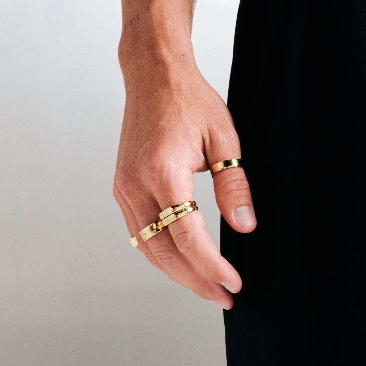 Men's Gold Serenity Ring in 18k gold infused stainless steel, worn on the thumb, hand hanging by his side, black pants
