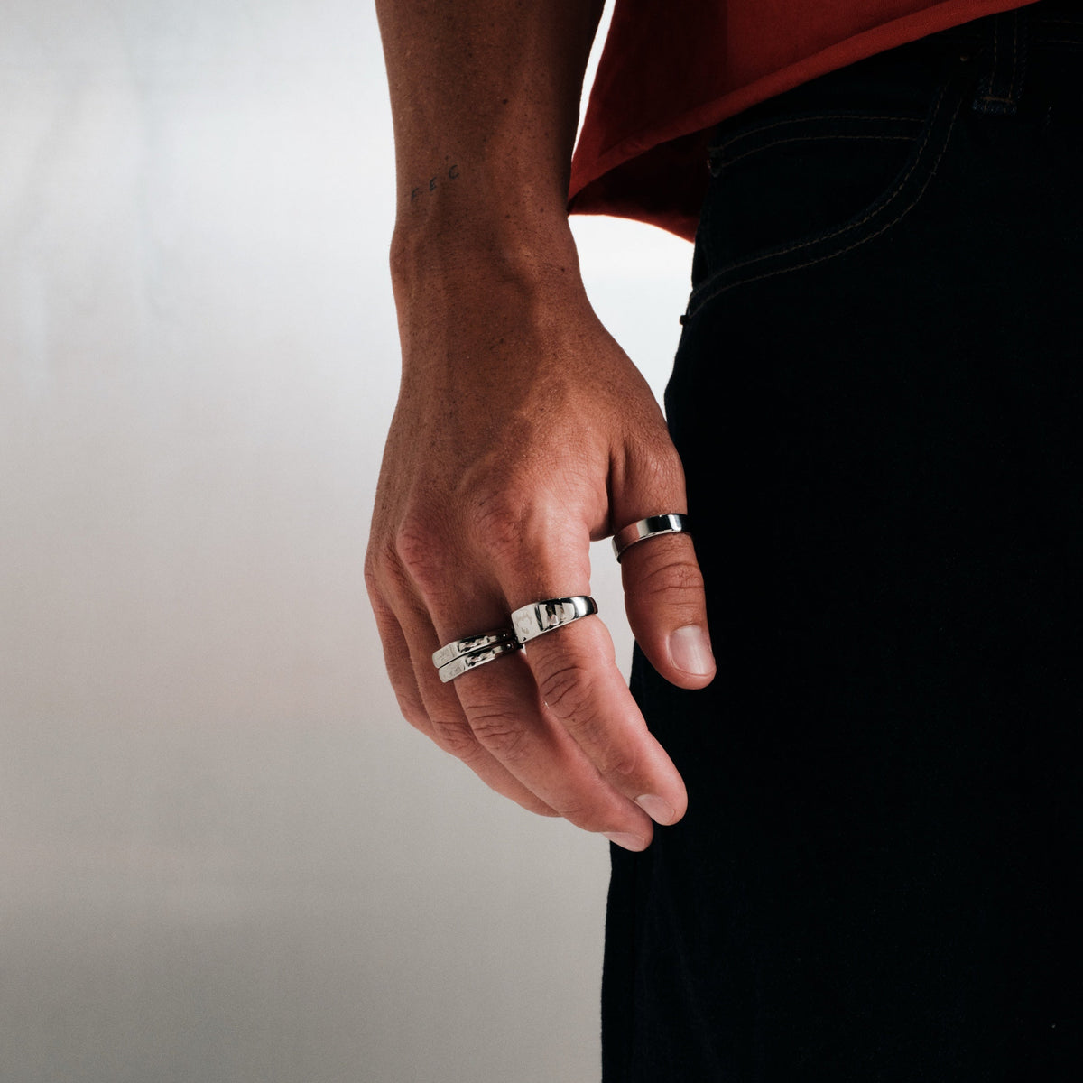 Men's Serenity Ring in 316L stainless steel, silver finish, worn on the thumb, hand hanging by his side, red tee, black jeans