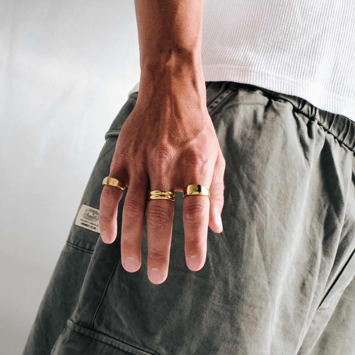 Men's Gold Stacker Rings in 18k gold infused stainless steel, both worn on the middle finger, hand relaxed at his side