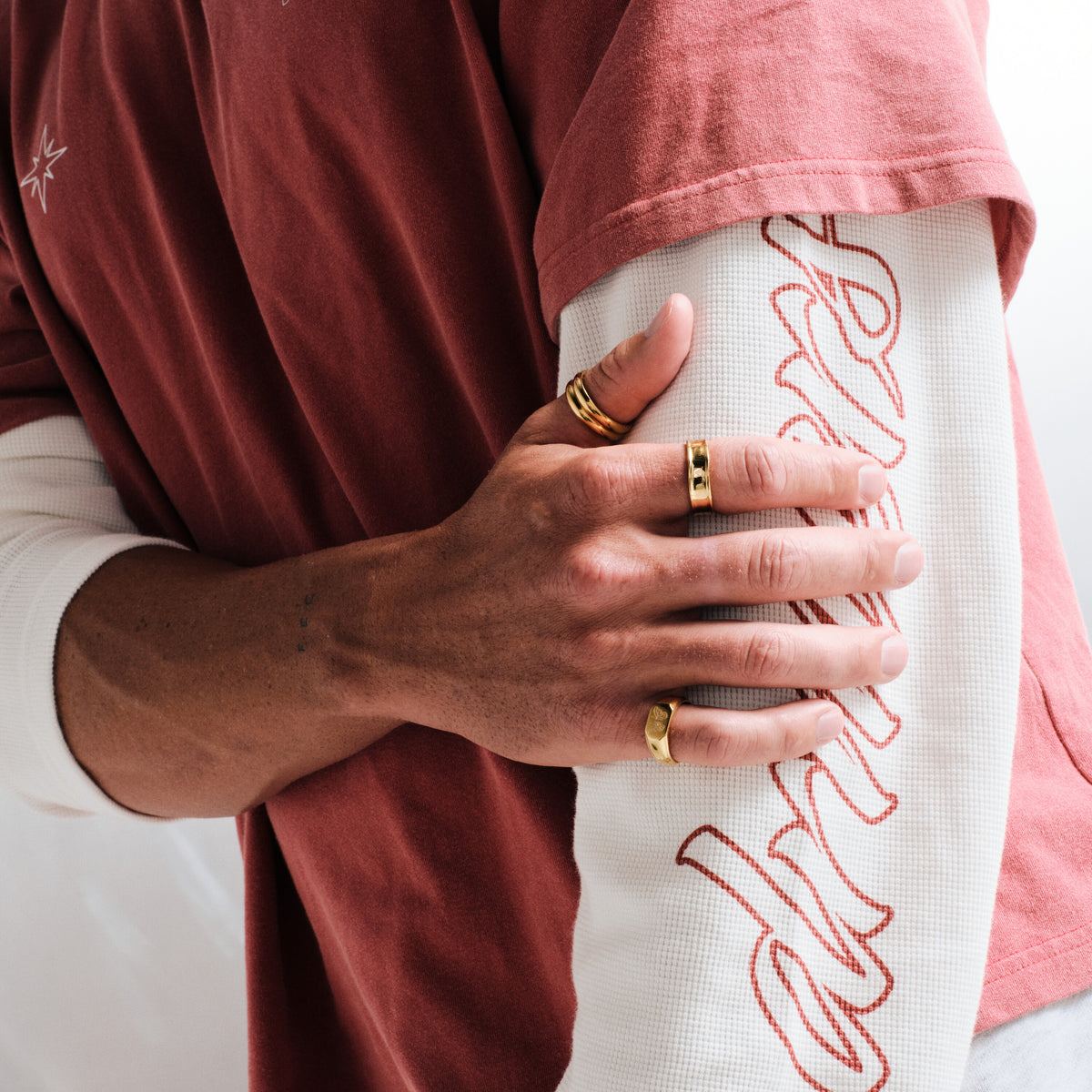 Men's Gold Stacker Rings in 18k gold infused stainless steel, both worn on his right thumb, hand gripping his upper arm