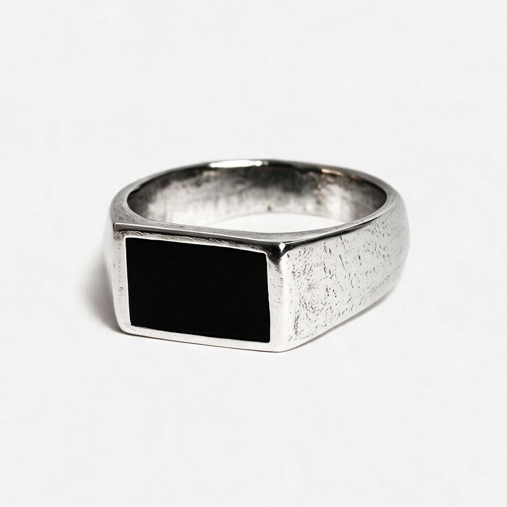 A silver signet ring with a textured band and a rectangular black inlay, photographed on a clean white background.