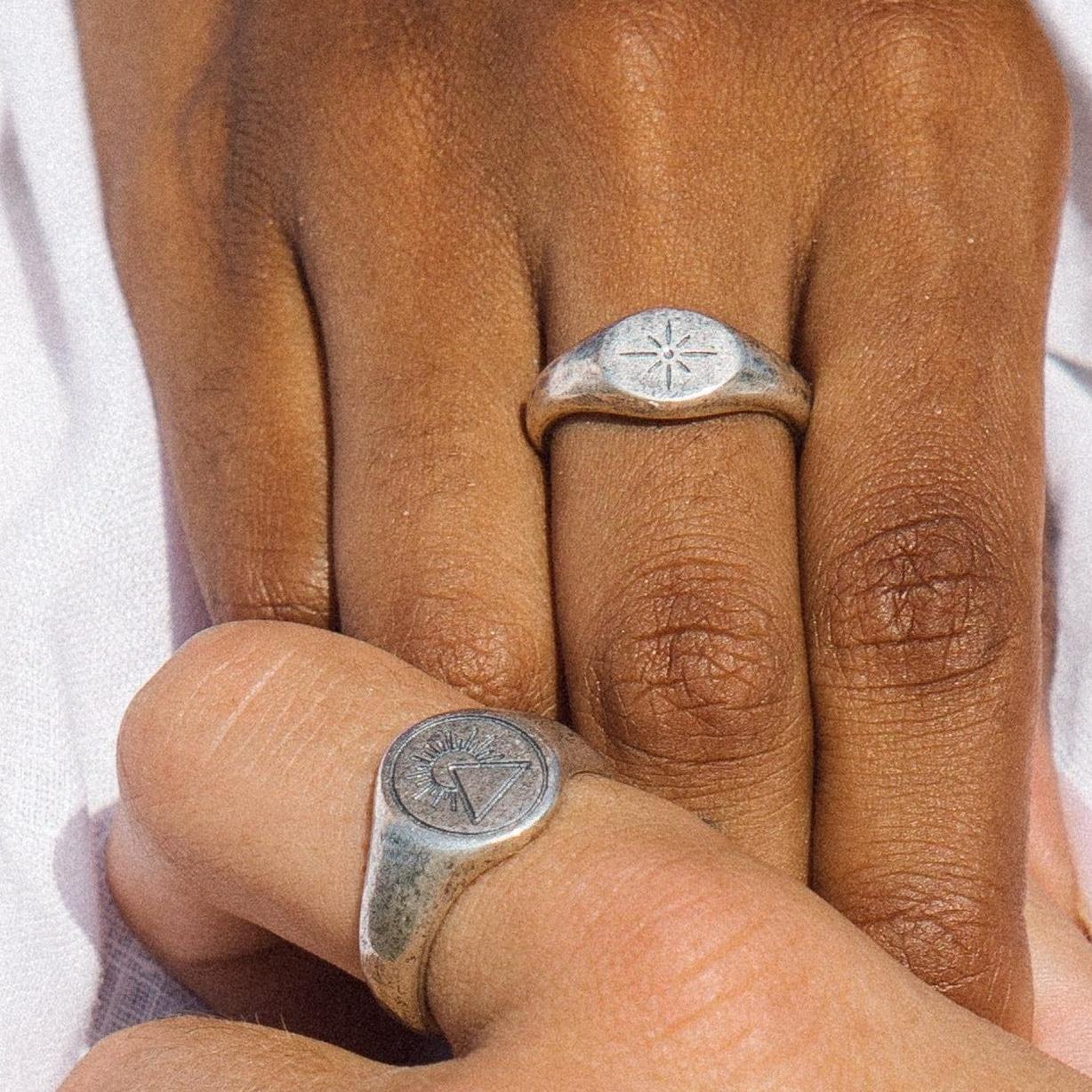 Close-up of two hands showing the Billie Jo Luminous Ring on one finger and another silver signet ring on the thumb. Men's jewellery styling.