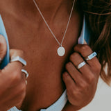 A close-up of a woman wearing the Billie Jo Untold Pendant, a sterling silver necklace with a round, textured pendant, styled with multiple silver rings.