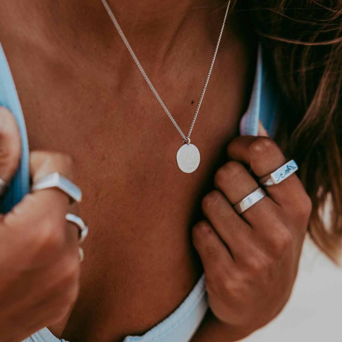 A close-up of a woman wearing the Billie Jo Untold Pendant, a sterling silver necklace with a round, textured pendant, styled with multiple silver rings.