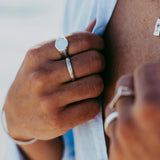 A close-up lifestyle image of a man adjusting his shirt, showcasing a selection of sterling silver Billie Jo Stacker Rings with varied textures and designs.
