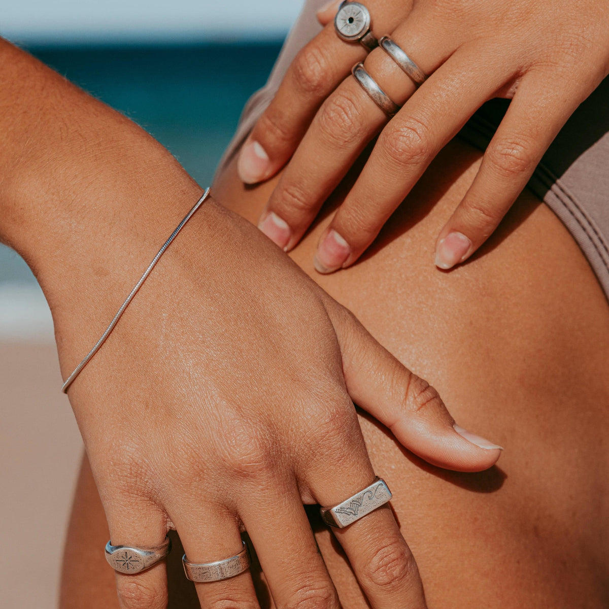 Close-up of a man's hands resting on his leg, wearing the sterling silver Billie Jo Snake Bracelet and a collection of the brand's signature rings. This on-hand shot highlights the bracelet's texture and how it can be styled.