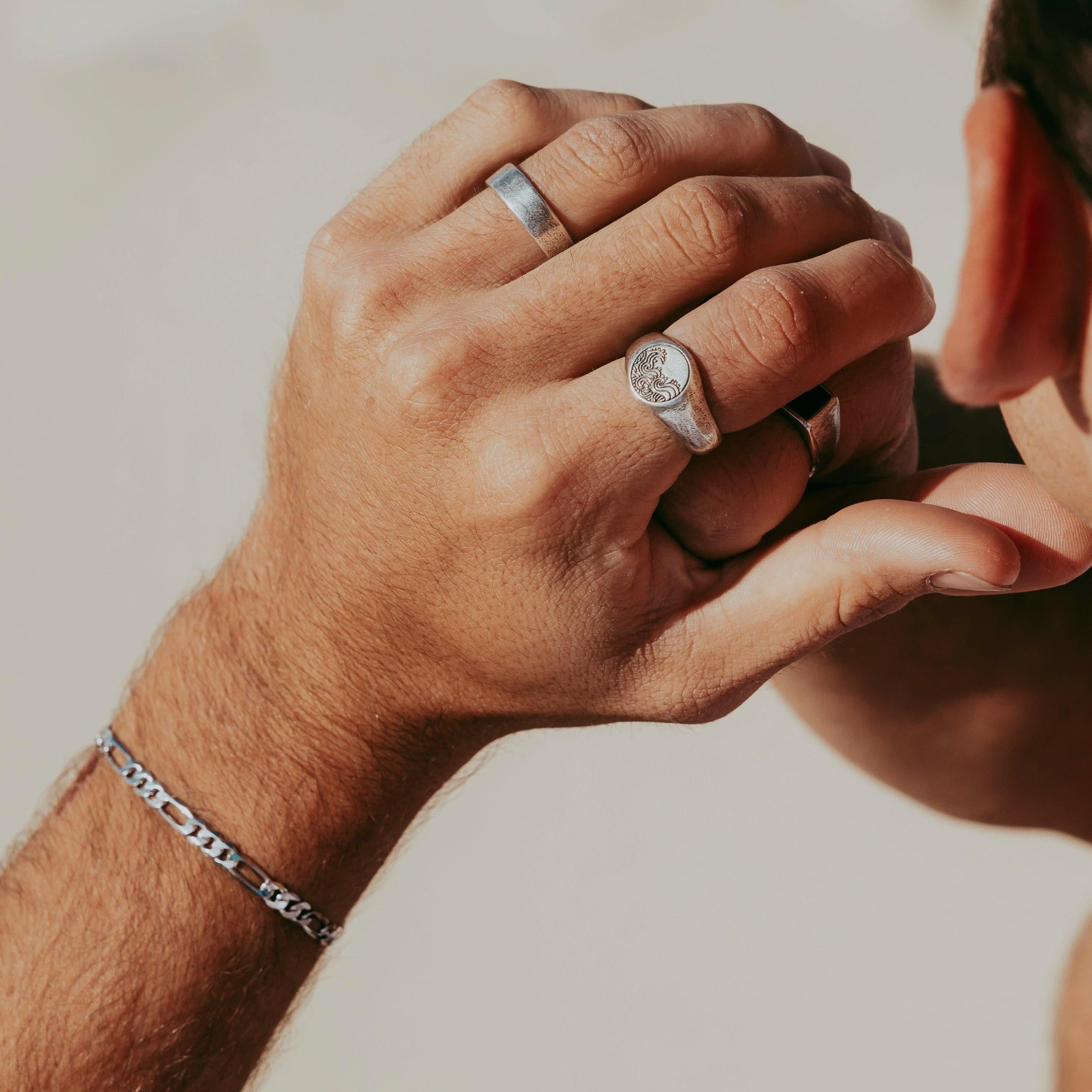 A man wearing the Billie Jo Figaro Bracelet in sterling silver, paired with a signet ring and band. This on-hand lifestyle shot shows the bracelet as part of a curated men's jewellery collection.