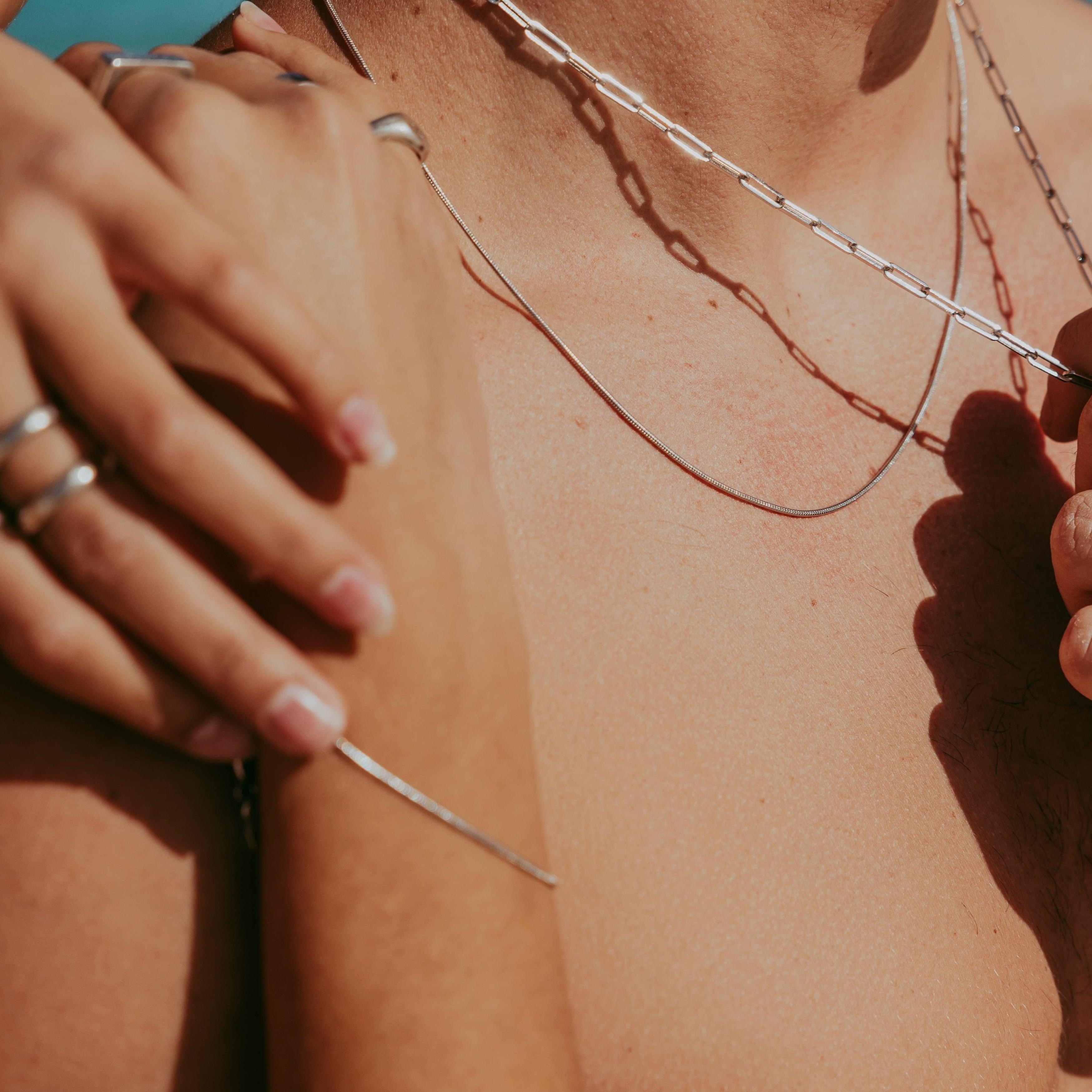 A man wearing the Billie Jo Snake Necklace in sterling silver, layered with other chains for a modern, masculine look. His hand, adorned with silver rings, rests on his chest.