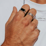 A man's hand wearing the Billie Jo Onyx Ring on his index finger, styled with other silver rings and a silver chain.