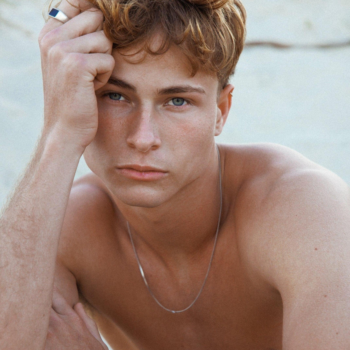 A male model with blue eyes and wavy brown hair wears the silver Curb Necklace by Billie Jo, showcasing its versatile and timeless appeal.
