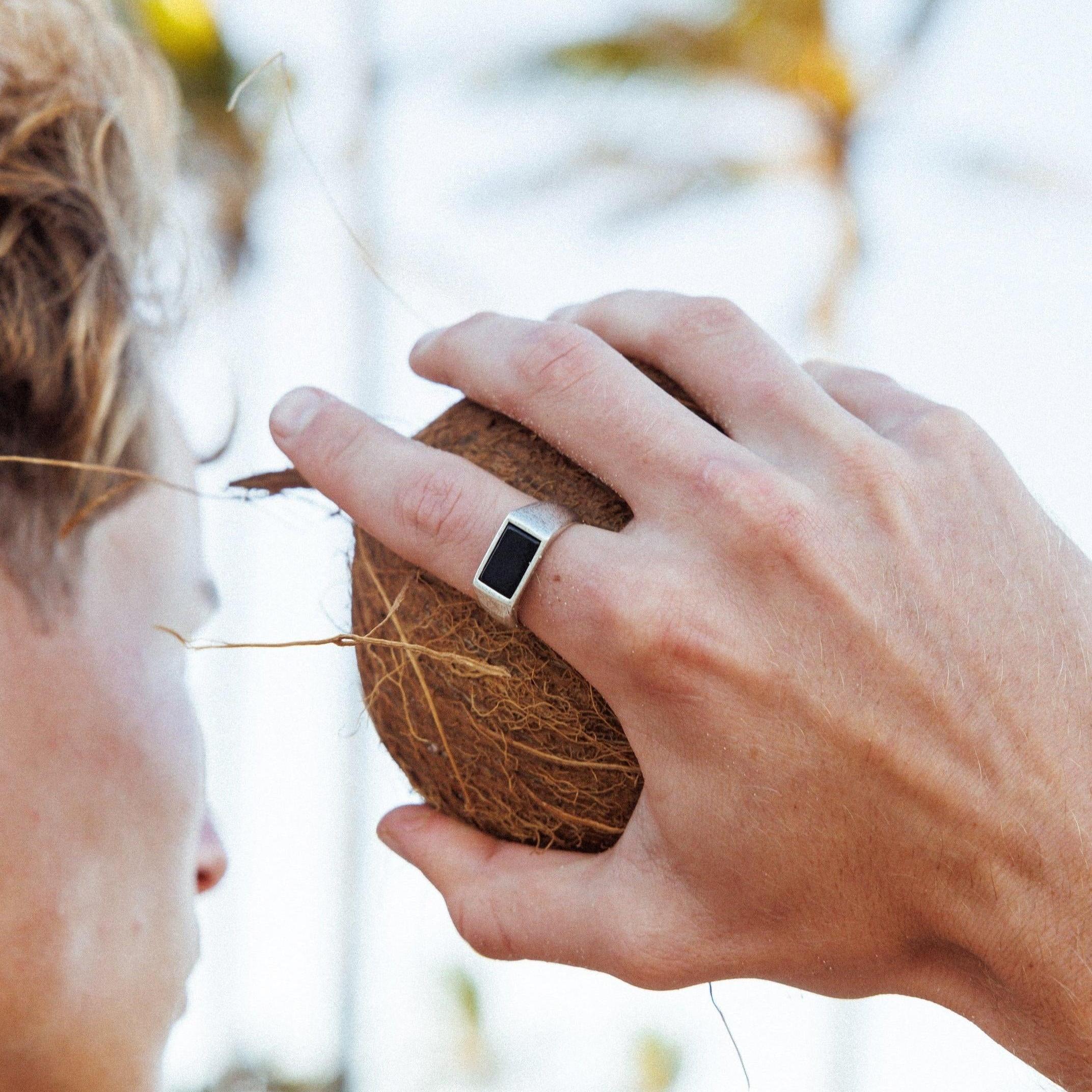 A man holding a coconut, with the Billie Jo Onyx Ring on his finger.