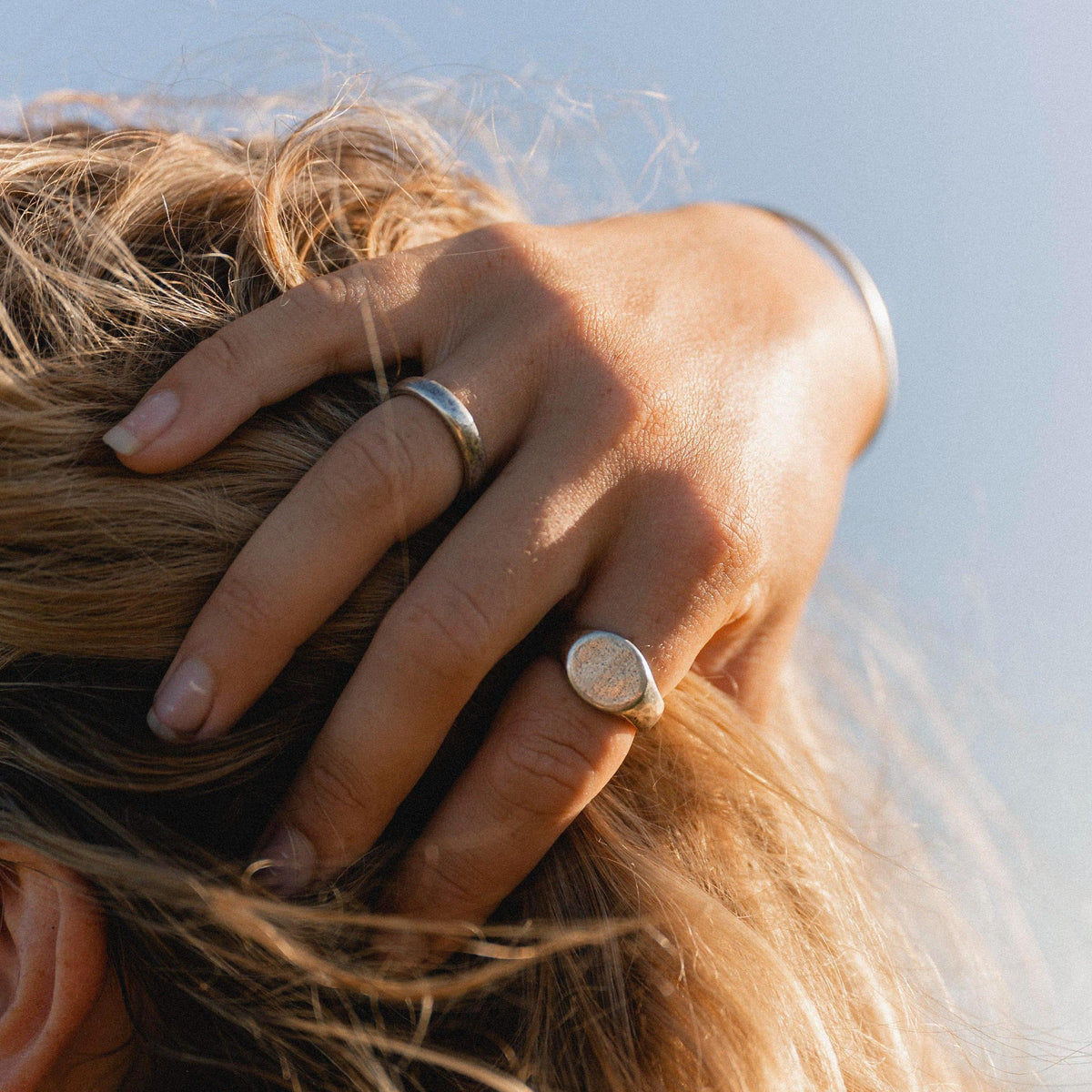A lifestyle shot of a woman's hand with the Billie Jo Signet Ring, her fingers running through her blonde hair in the sun.